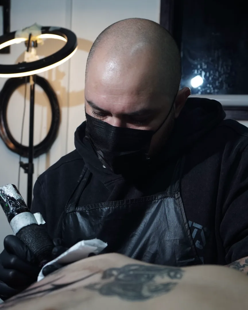 Miguel Muñoz (Anyeloski) tatuando en su taller, máquina en mano bajo el aro de luz